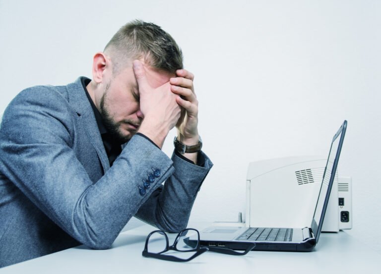 A man holds his head in his hands in front of a laptop.