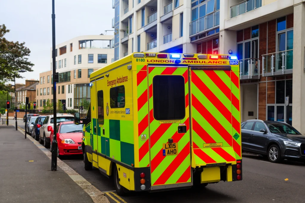 An ambulance with flashing blue lights on a road in Greater London