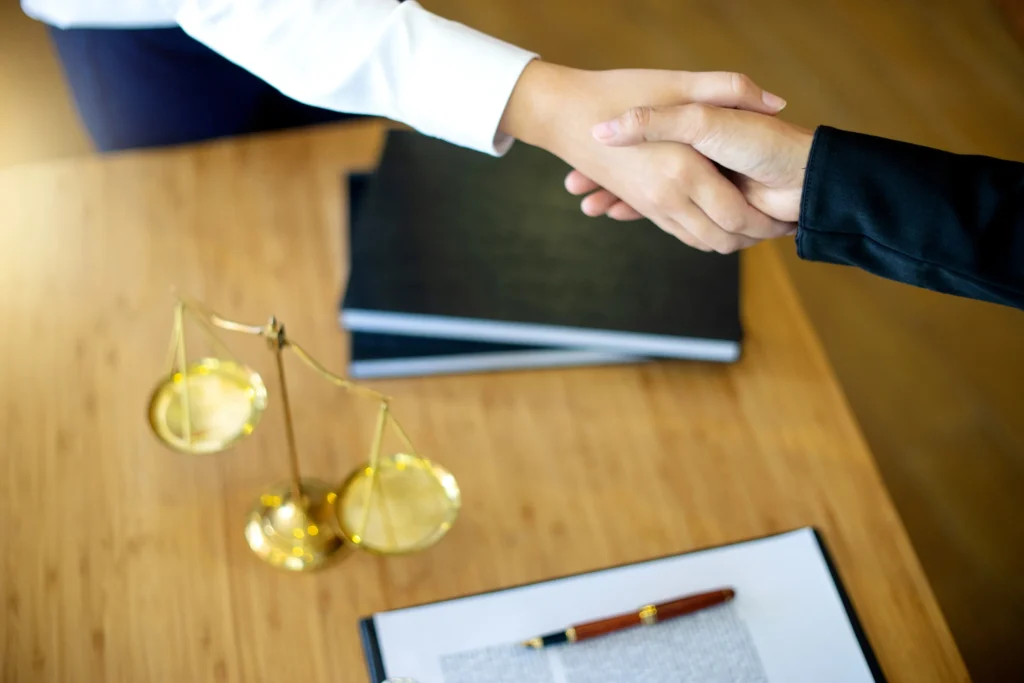 A solicitor shakes hands across a wooden table with justice scales on it.